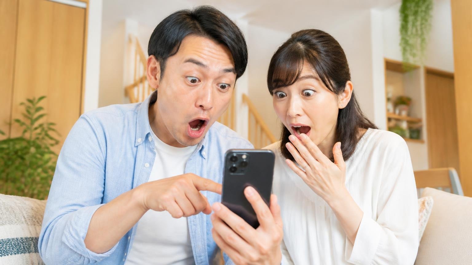 口コミ105件の評価分布|★1はたった1件だった 木造戸建てのリビングでスマホの口コミ画面を見る夫婦2人 驚いた表情