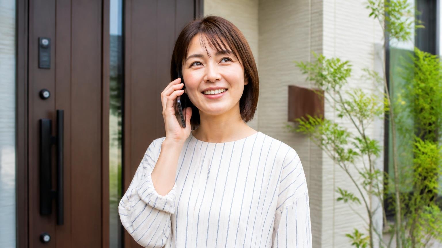 まず無料見積もりを取りたい駆除業者。玄関前でスマホを手に電話をかける女性1人が前向きな表情