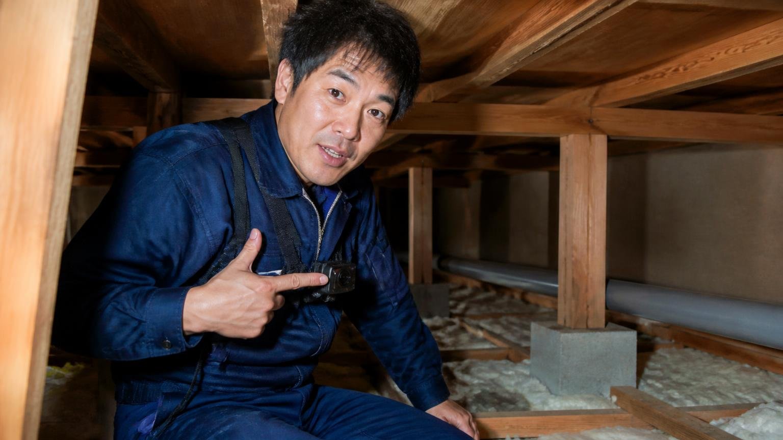 作業中をカメラで撮影してくれた。木造戸建ての薄暗い天井裏で、作業員1人が胸の小型カメラを指さして住人に説明する