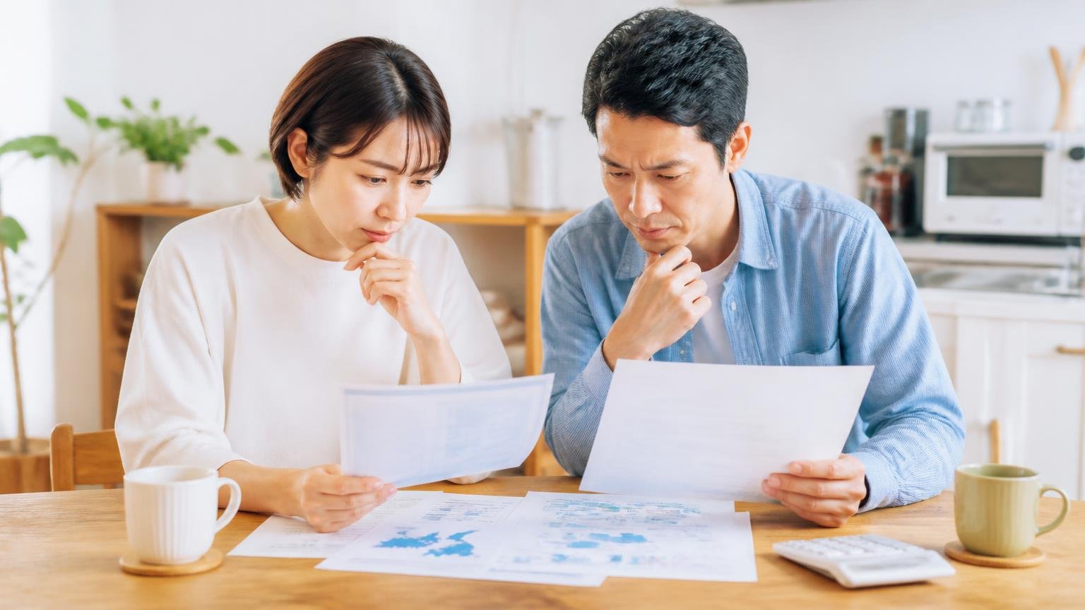 対応エリアと保証内容を確認する。ダイニングテーブルで資料を見比べる30代女性と40代男性の夫婦