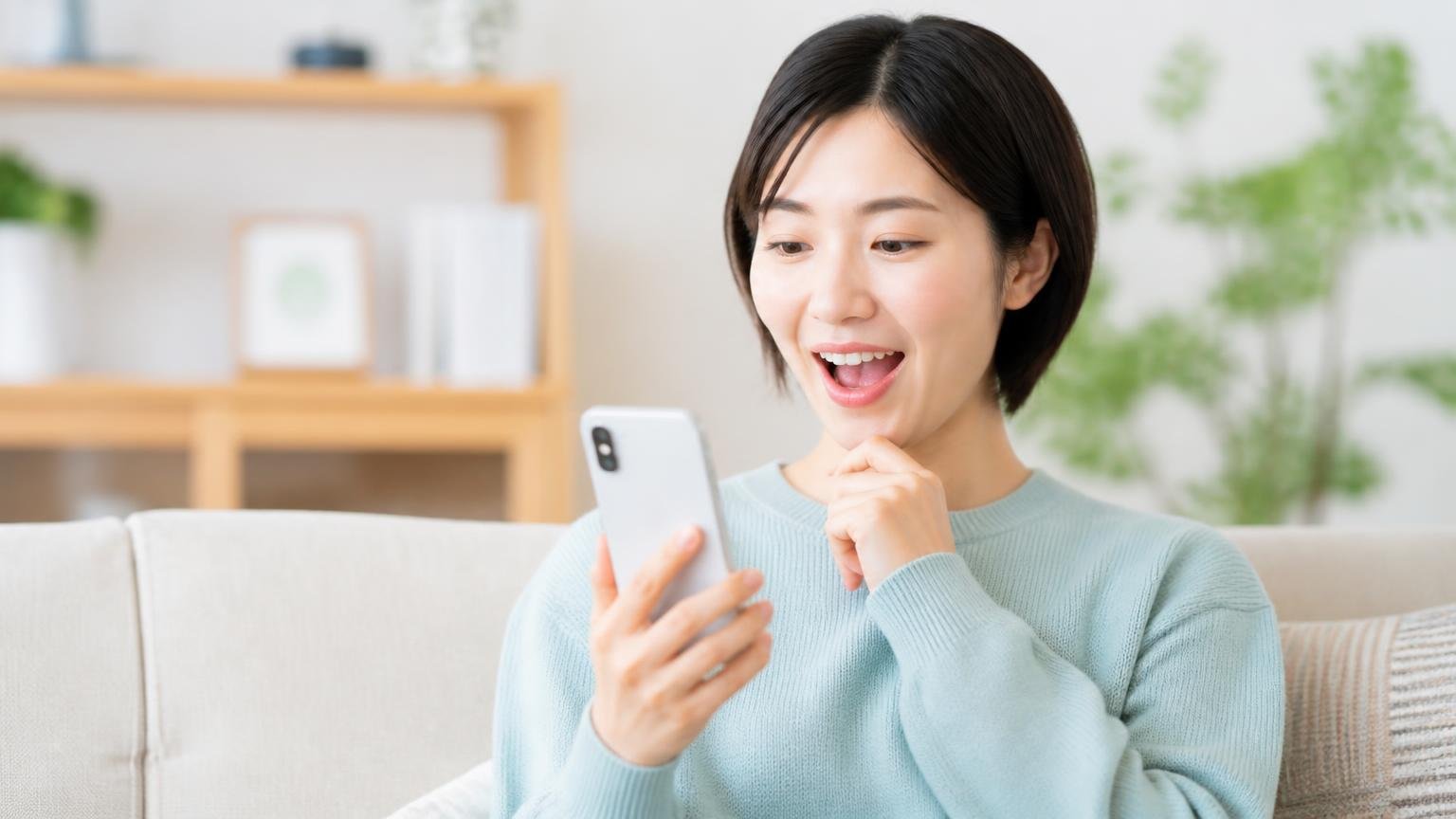 口コミへの企業の返信を確認する場面 リビングのソファでスマホ画面を見る女性1人 感心した表情