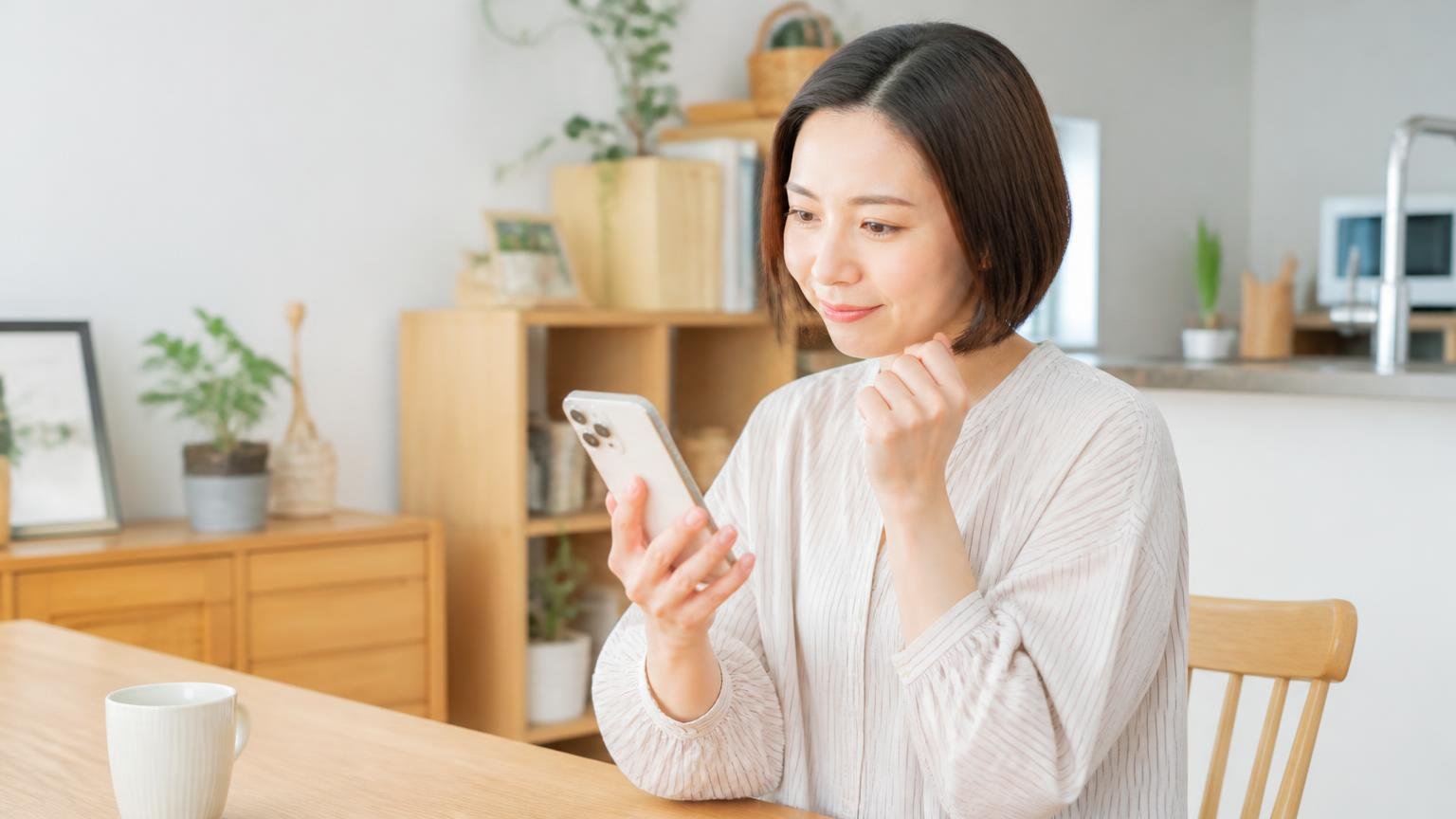 料金表を公開しているか確認する 自宅のダイニングでスマホの料金ページを見る30代女性がうなずく
