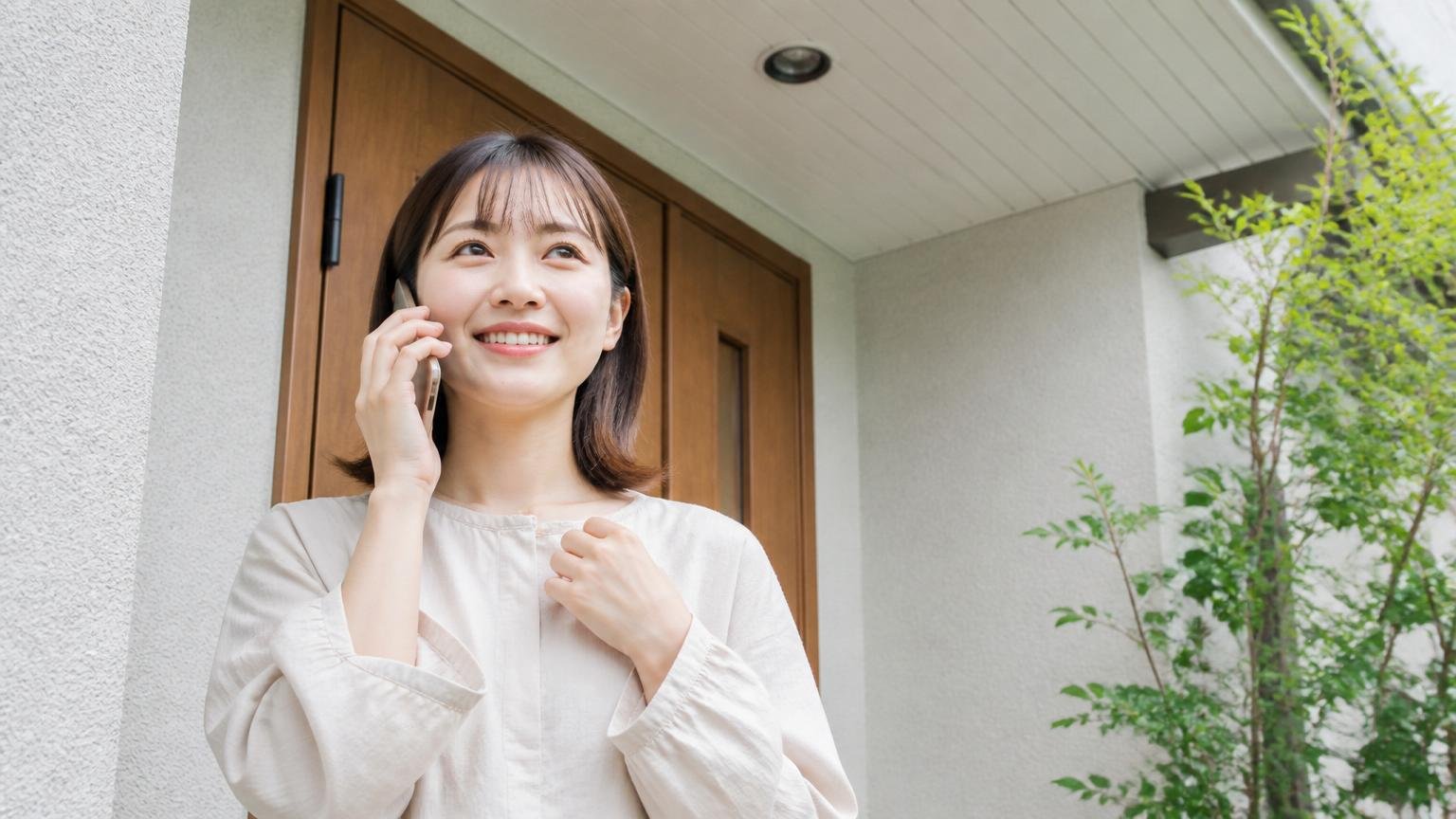 キャンセルしても丁寧だった電話対応。家の軒下を見上げる玄関前で30代女性がスマホで相談し安心した表情