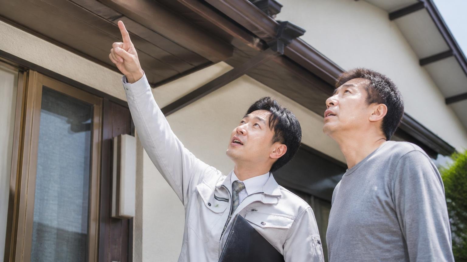 「〜円から」は最も条件の良い現場の金額でしかない 家の軒下を見上げて指をさす作業員と住人の2人 説明する表情