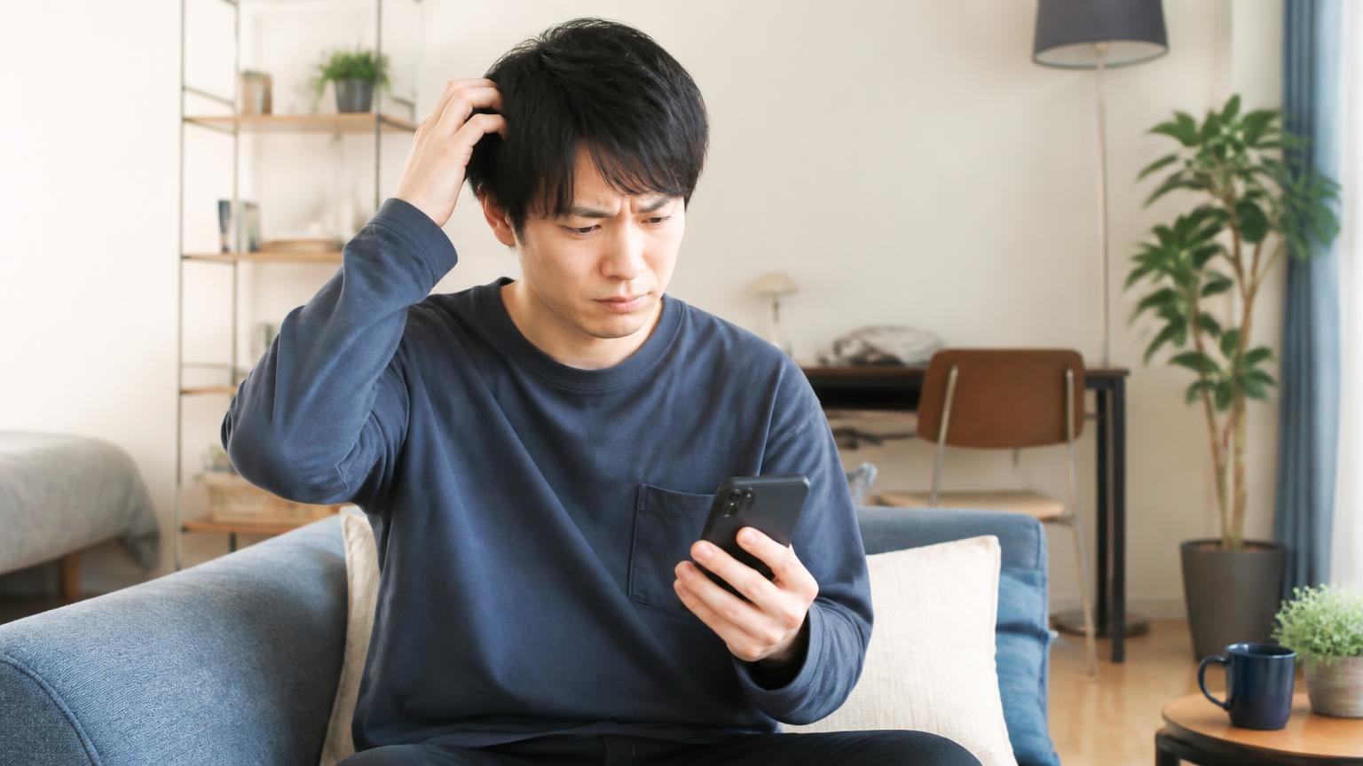 向いていない人の4つの条件。マンションの一室でスマホを見る20代男性1人が困り顔で頭をかく