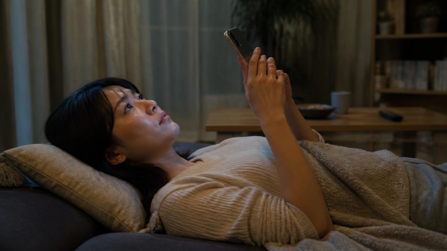 深夜に相談したい人には向かない。深夜のリビングで天井を見上げスマホを握る30代女性