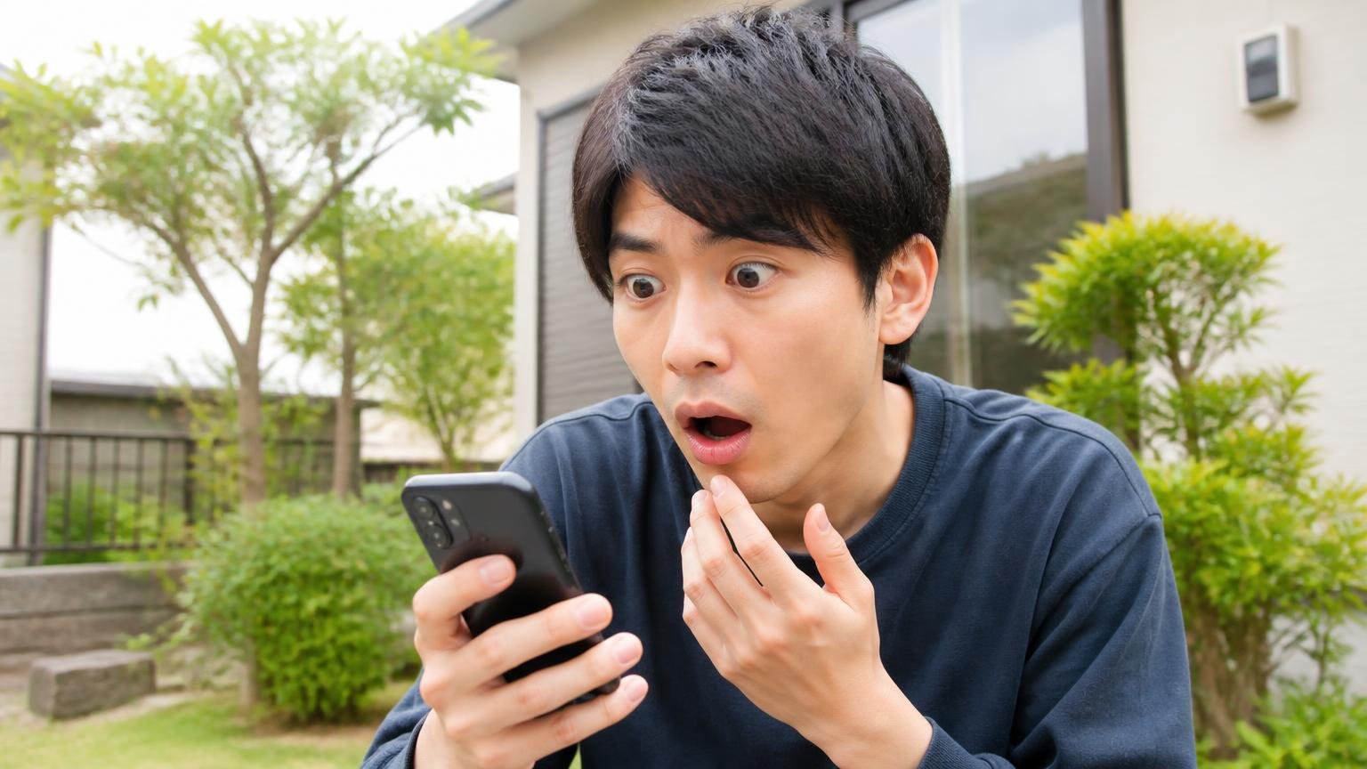 害獣の種類で対応が変わることを知る場面。住宅の庭先でスマホを見ながら驚く表情の20代男性1人