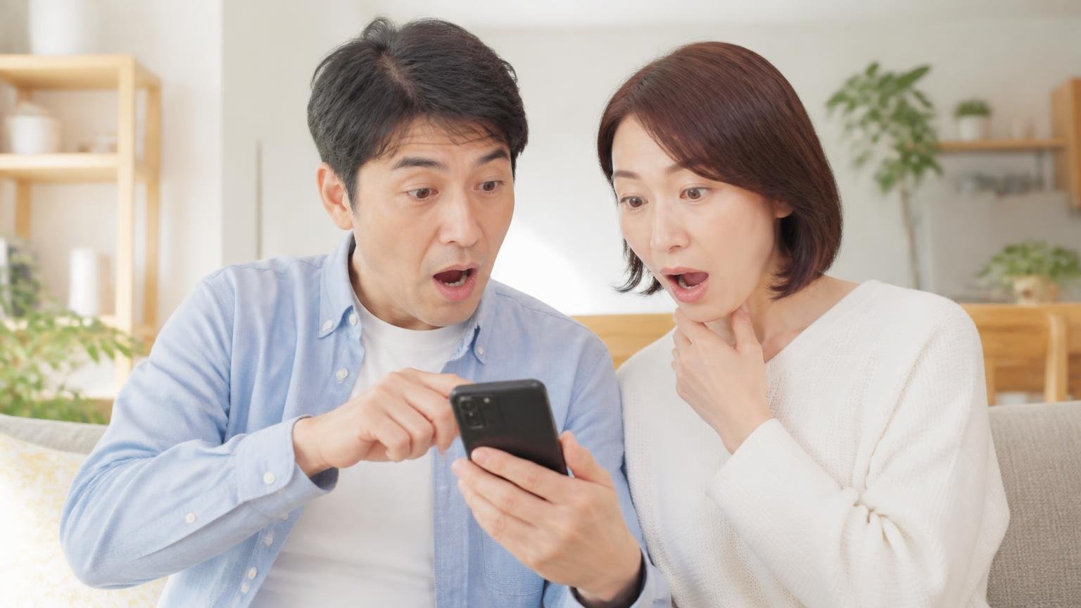 公開口コミ38件に低評価なし。リビングでスマホの口コミ一覧を見つめる40代夫婦2人が驚く表情
