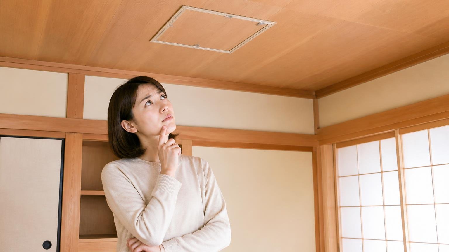 賛否が割れる理由を探る場面。木造戸建ての和室で天井の点検口を見上げる30代女性が首をかしげて考え込む