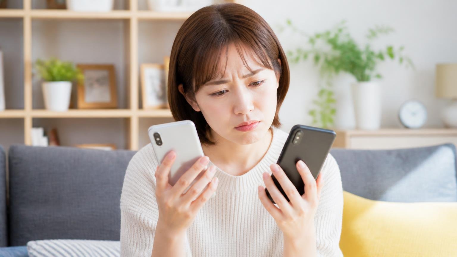 楽天とAmazonの評価差｜自宅リビングで女性1人がスマホのレビューを見比べ眉をひそめる