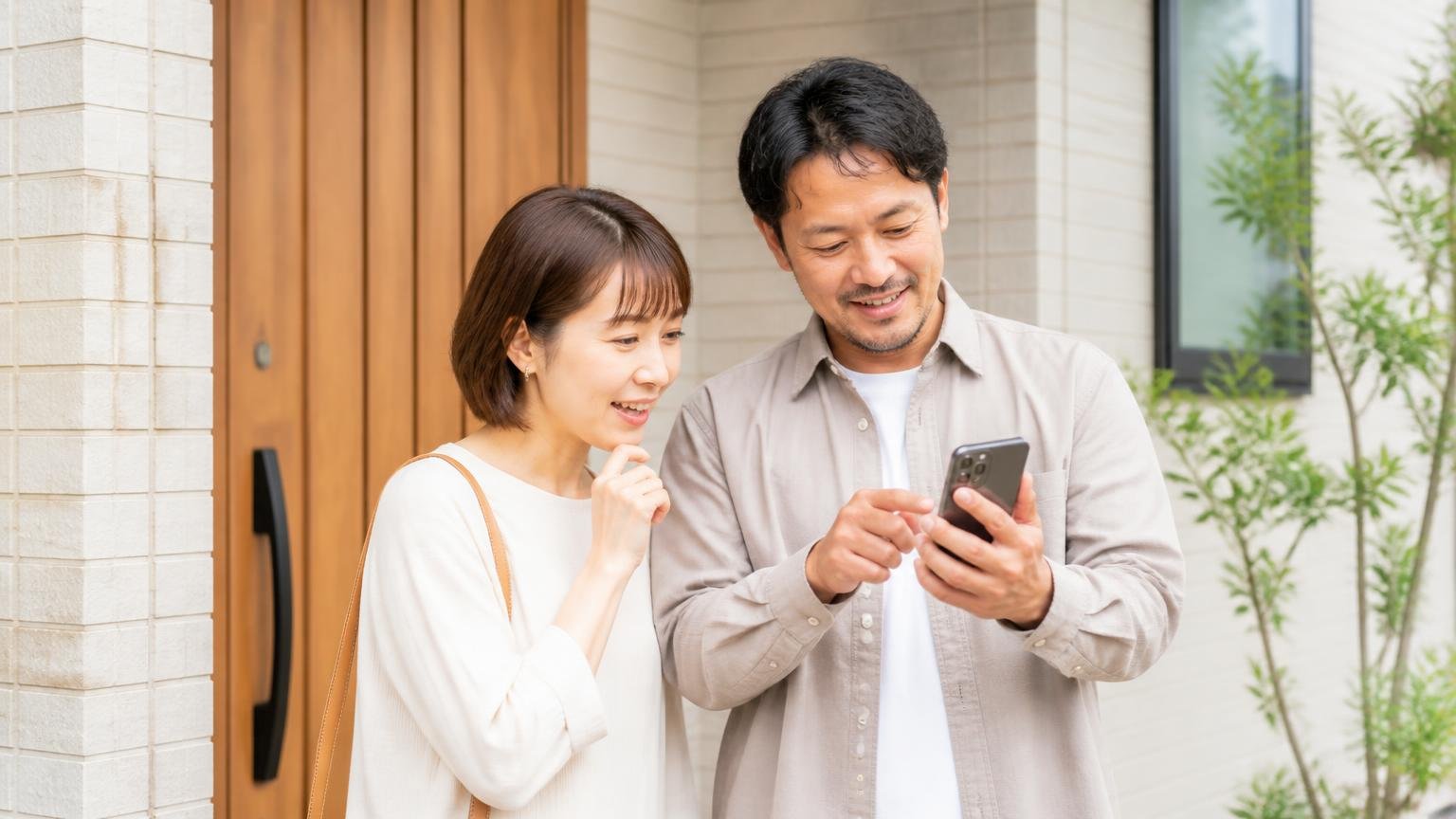 まず無料で見てもらった窓口|玄関前でスマホを手に問い合わせを始める30代夫婦2人