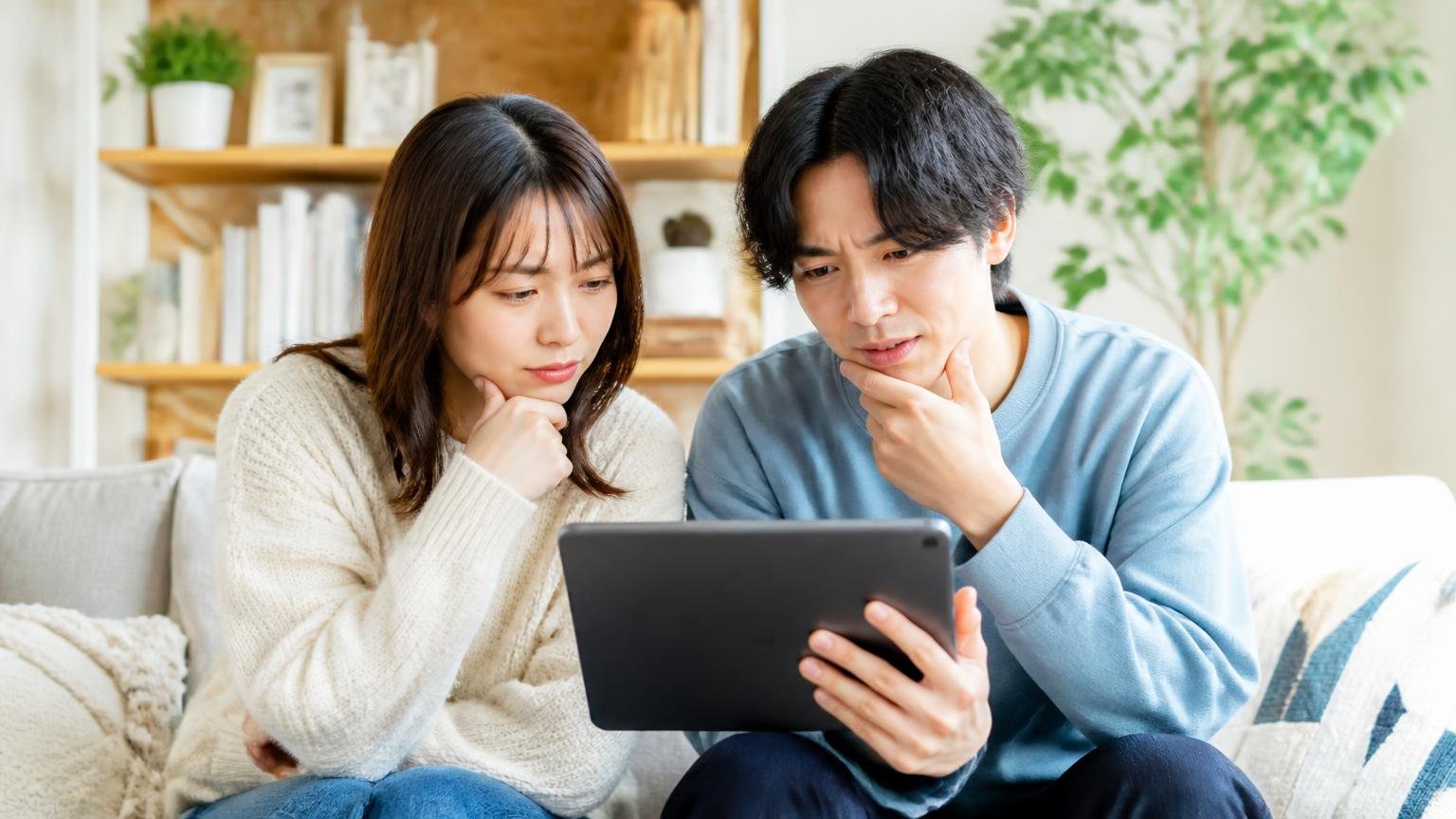 まず知っておきたい口コミの読み方2つ。リビングのソファでタブレットを見比べる30代女性と20代男性の2人