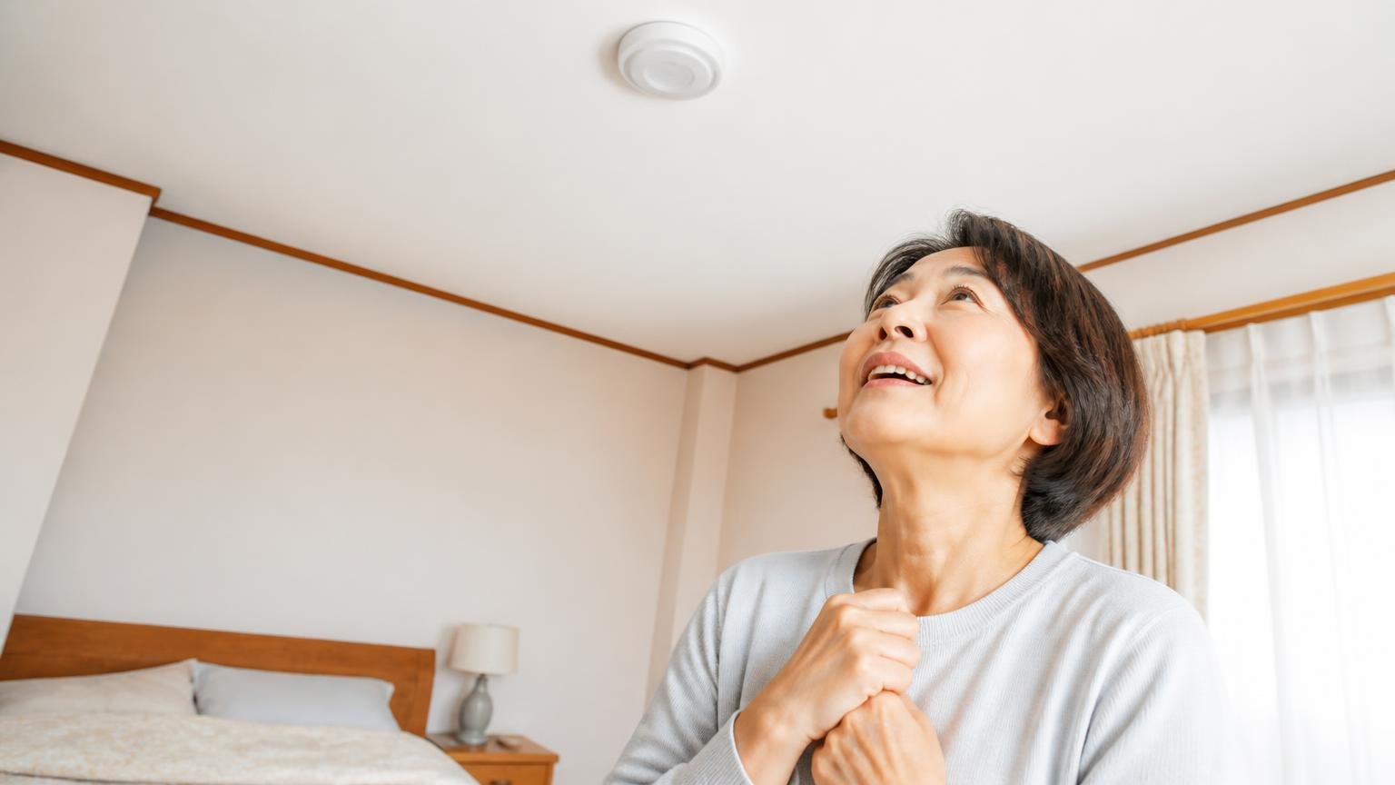 設置4日で物音が止まった。木造戸建ての寝室で天井を見上げ安堵の表情を浮かべる50代女性