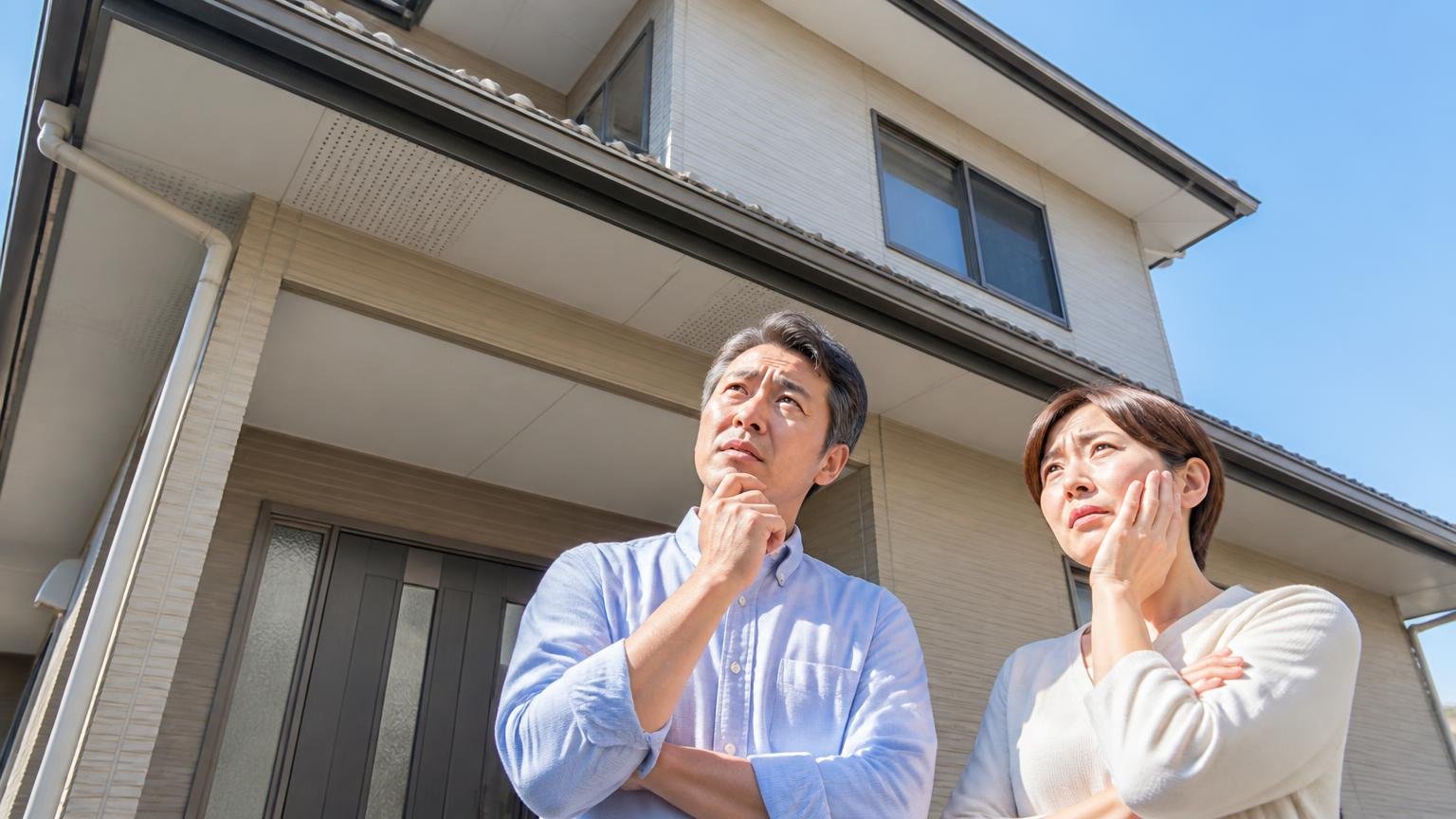 向いていない人の条件 二階建て住宅の屋根と軒天を地上から見上げる住人2人 困った表情で相談