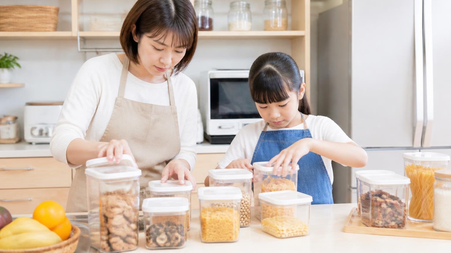 部屋のエサを片づける。住宅の台所で食品をフタつき容器にしまう主婦1人と子ども1人が真剣な表情