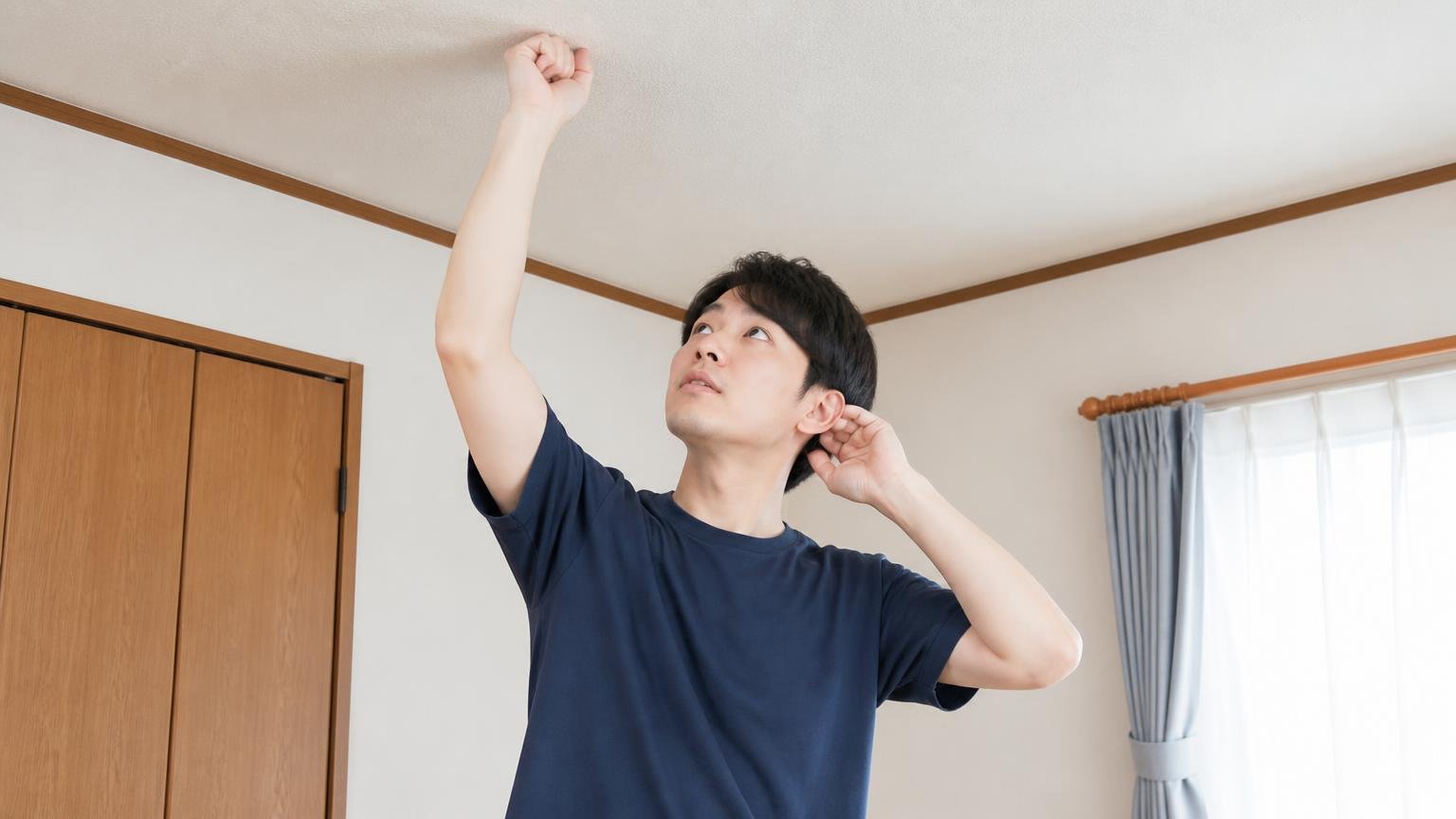 天井を叩いて反応を見る。木造戸建ての2階居室で天井を軽く叩く20代男性1人が耳を澄ませる