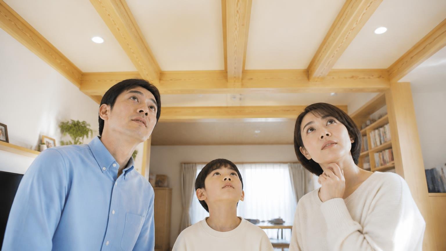 家鳴りは鳴るタイミングと場所に規則性がある 木造戸建てのリビングの天井 見上げる家族3人 落ち着いた表情