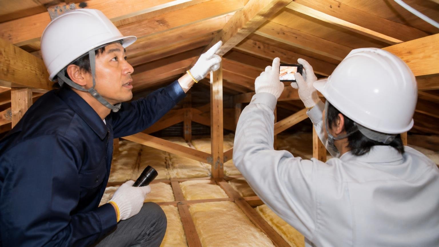 専門業者の作業の流れ。木造戸建ての天井裏で作業員2人が写真を撮りながら点検し説明する
