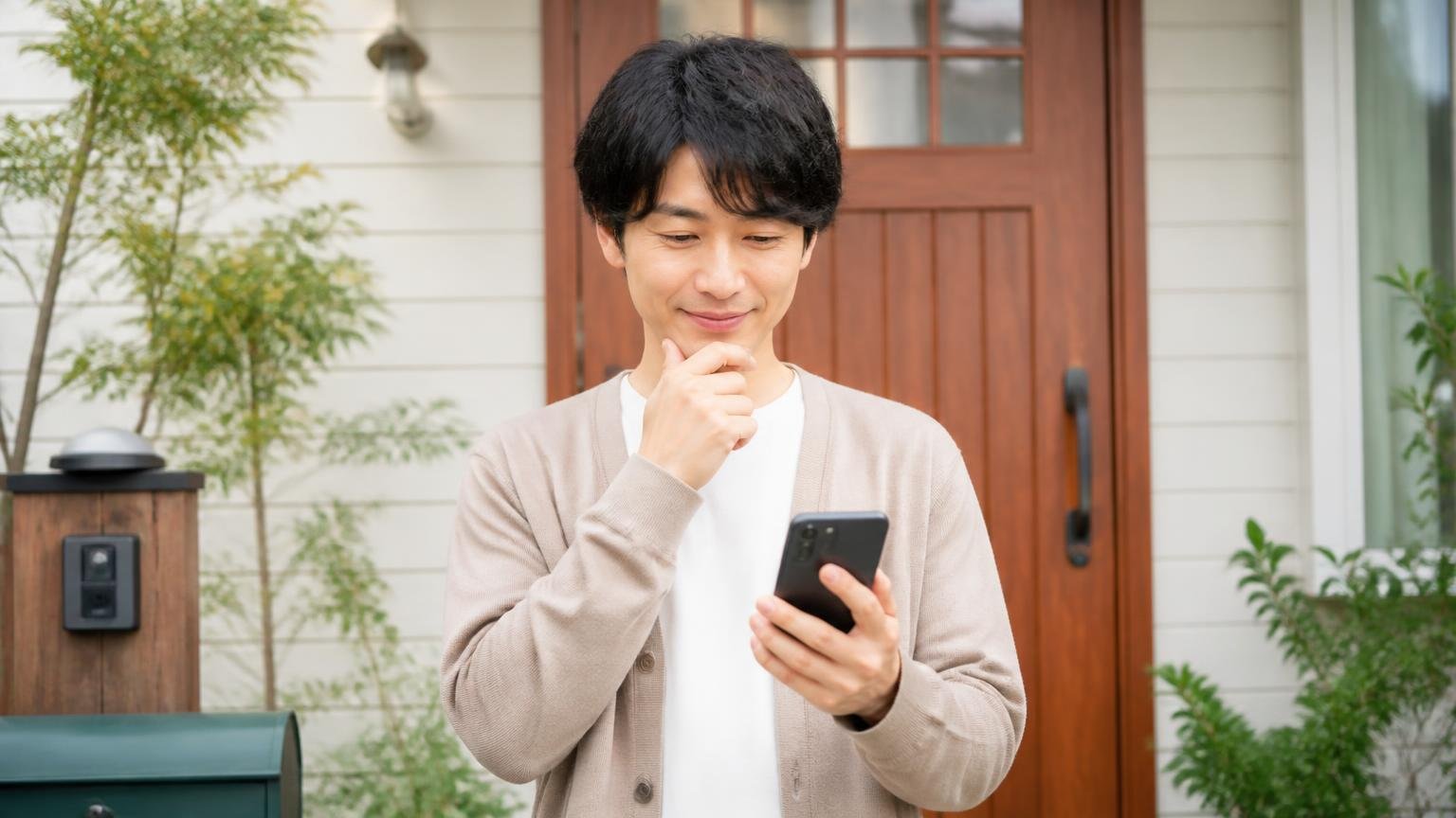 相談先の分岐は3つ どれでも間違いではない 木造戸建ての玄関先 スマホを手に考える住人1人 表情がやわらぐ